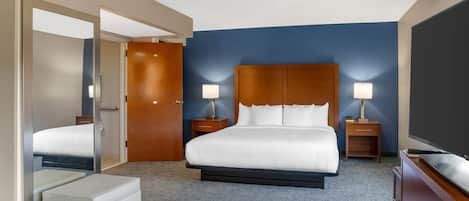 A hotel room with a large bed, two bedside tables with lamps, a wooden headboard, a flat-screen TV, and a small seating area.