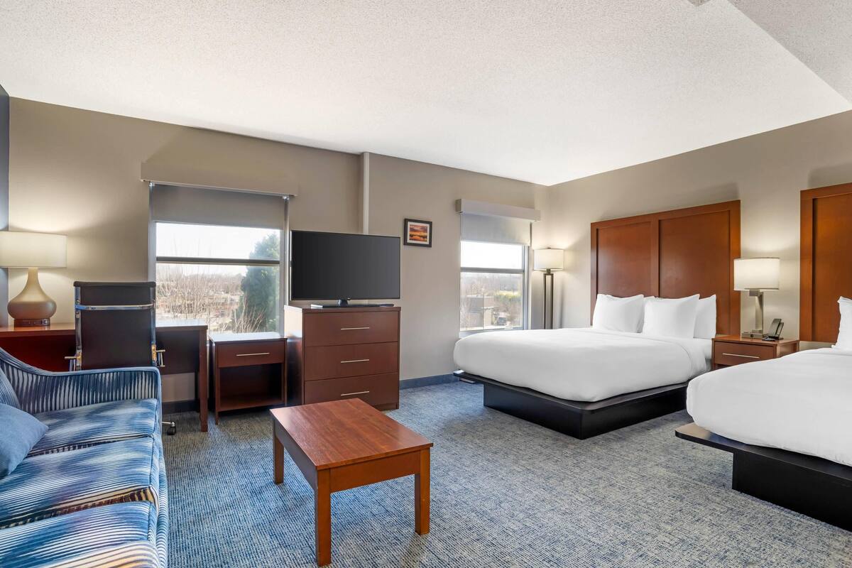 Une chambre d’hôtel avec deux lits, un bureau, une chaise, une télévision et une fenêtre donnant sur un paysage agréable.