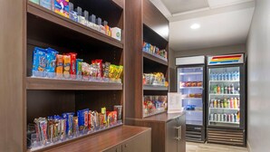 A snack bar with shelves stocked with various packaged snacks and a refrigerator with bottled beverages. - Comfort Suites near Birkdale Village- Huntersville (Huntersville)