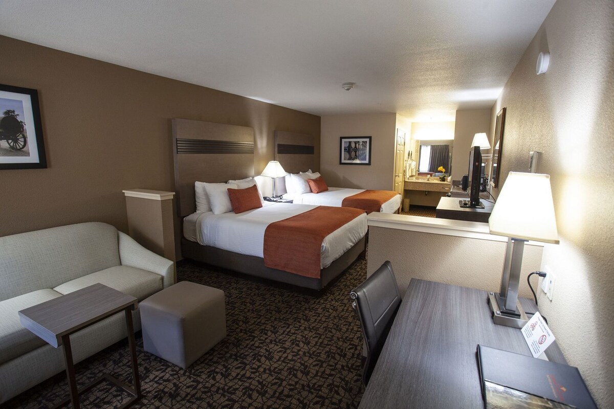 Ein Hotelzimmer mit einem Bett, zwei Nachttischen, einem Schreibtisch, einem Sessel und einem Spiegel.