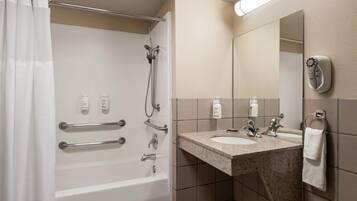 A bathroom with a bathtub, shower, and sink. There are handrails, a towel rack, and a mirror.