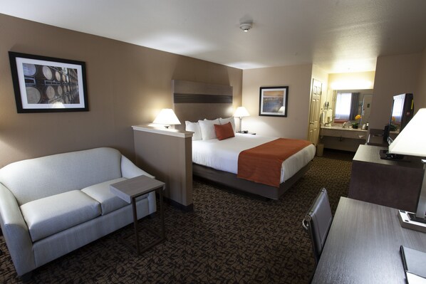 A hotel room with a bed, a sofa, a desk, and a mirror.