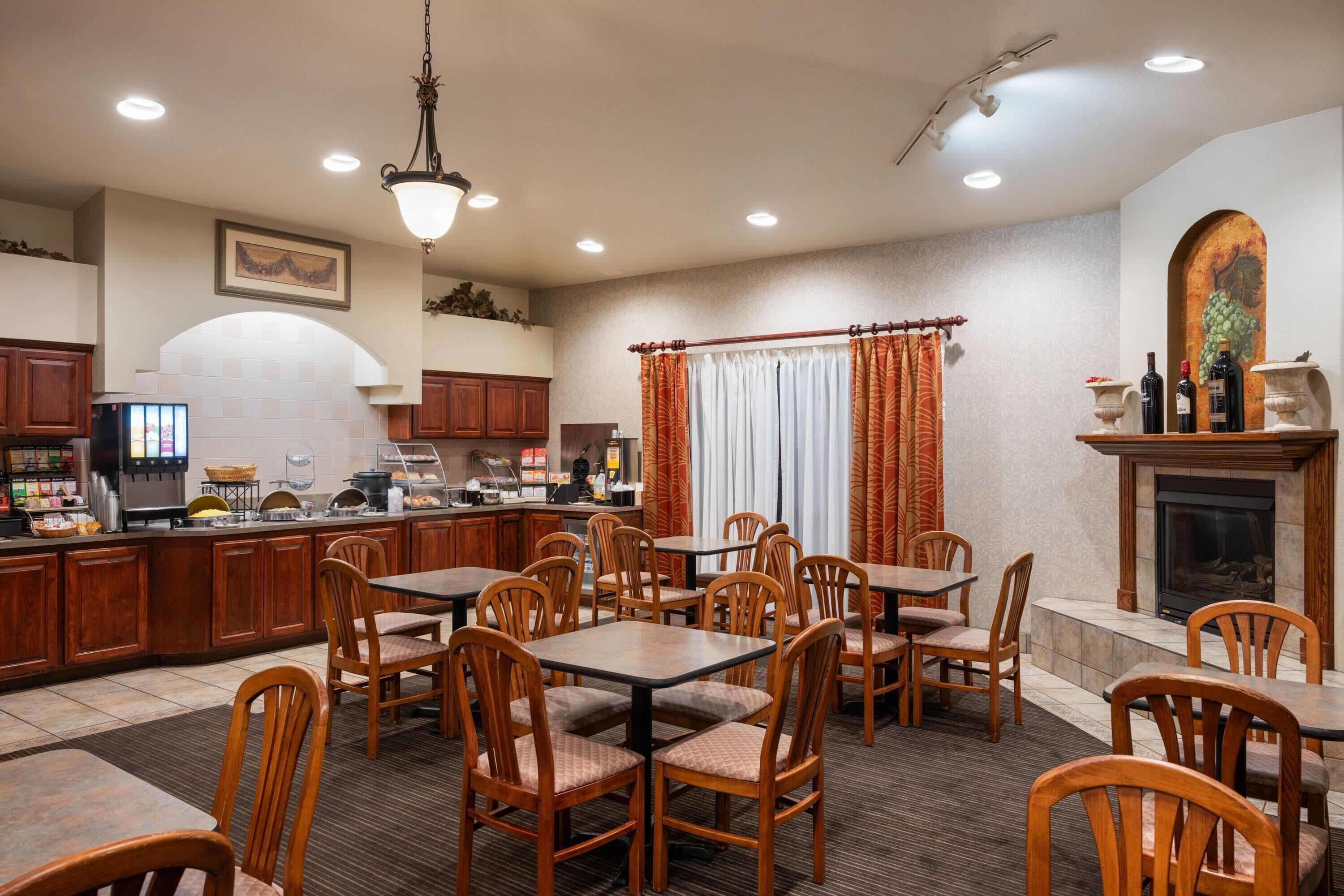 A restaurant with wooden tables and chairs, a counter with a coffee machine, and a fireplace.