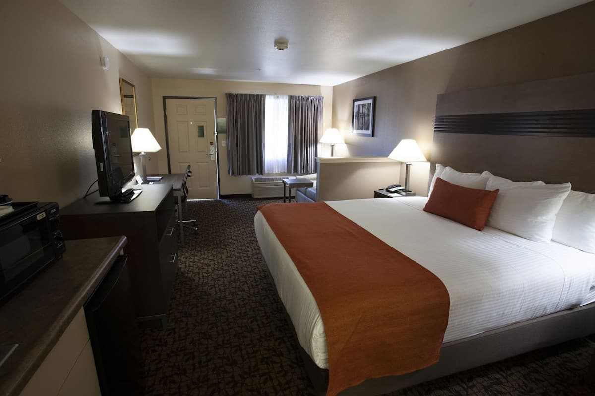 Ein Hotelzimmer mit Bett, Schreibtisch, Stuhl, Fernseher und einem Fenster mit Vorhängen.