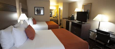Una habitación de hotel con dos camas, un escritorio con computadora, televisor y espejo.