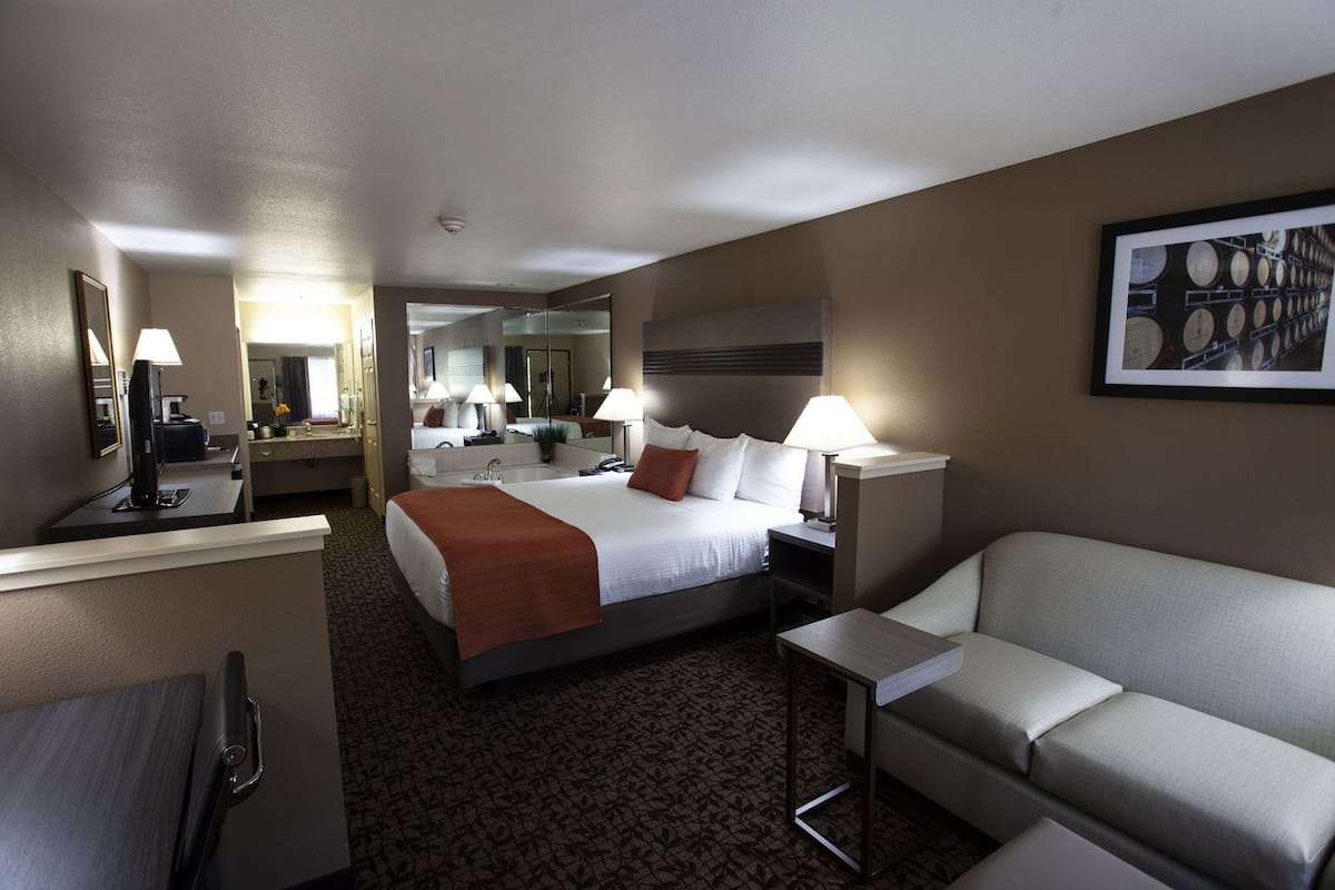 Ein Hotelzimmer mit Bett, Nachttisch, Lampe, Spiegel und einer Couch.