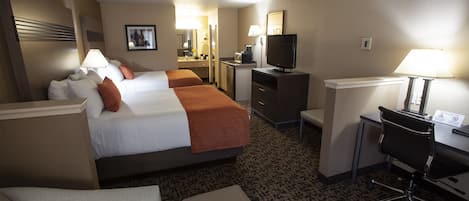 A hotel room with two beds, a desk, a chair, a TV, and a small kitchenette.