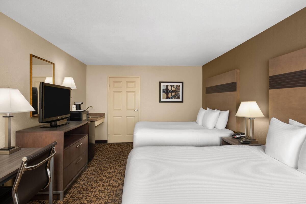 Une chambre d’hôtel avec deux lits, un bureau avec une télévision, une commode et une porte.