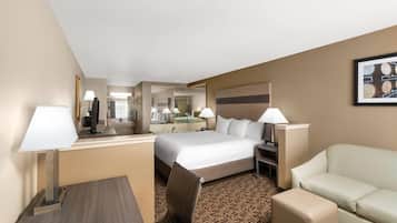 Quarto de hotel com cama, escrivaninha, cadeira, sofá e espelho.