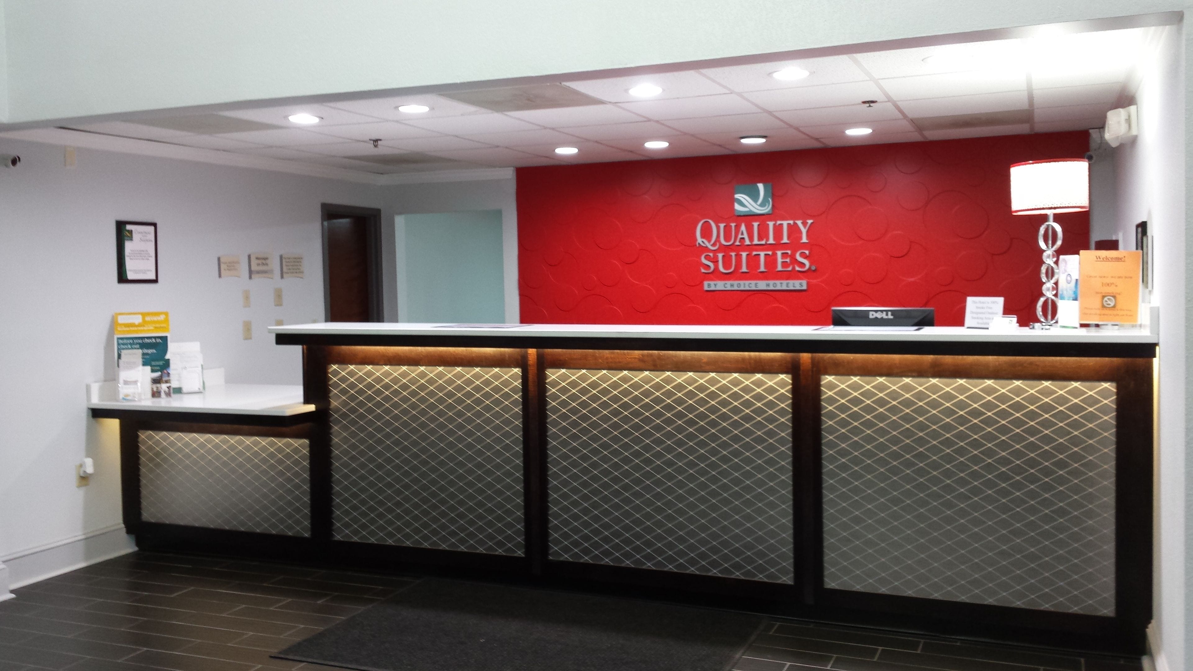 A hotel reception desk with a red wall, a Dell computer, and a welcome sign.