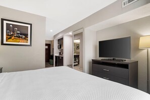 Habitación de hotel con una cama, televisión, escritorio con lámpara y un cuadro en la pared.