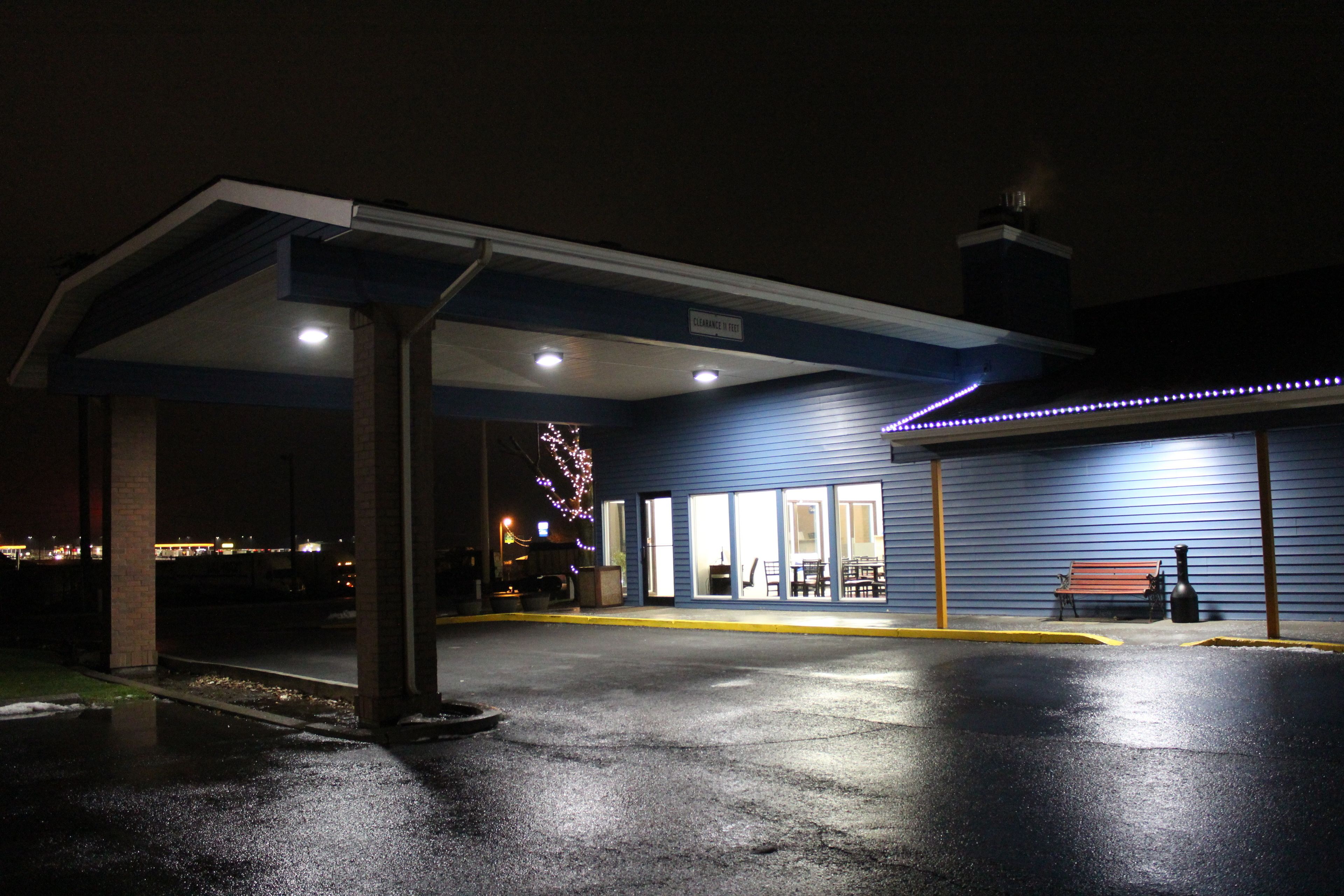 Eine Tankstelle bei Nacht mit überdachtem Bereich, einer Bank und einer Weihnachtsbaumdekoration.