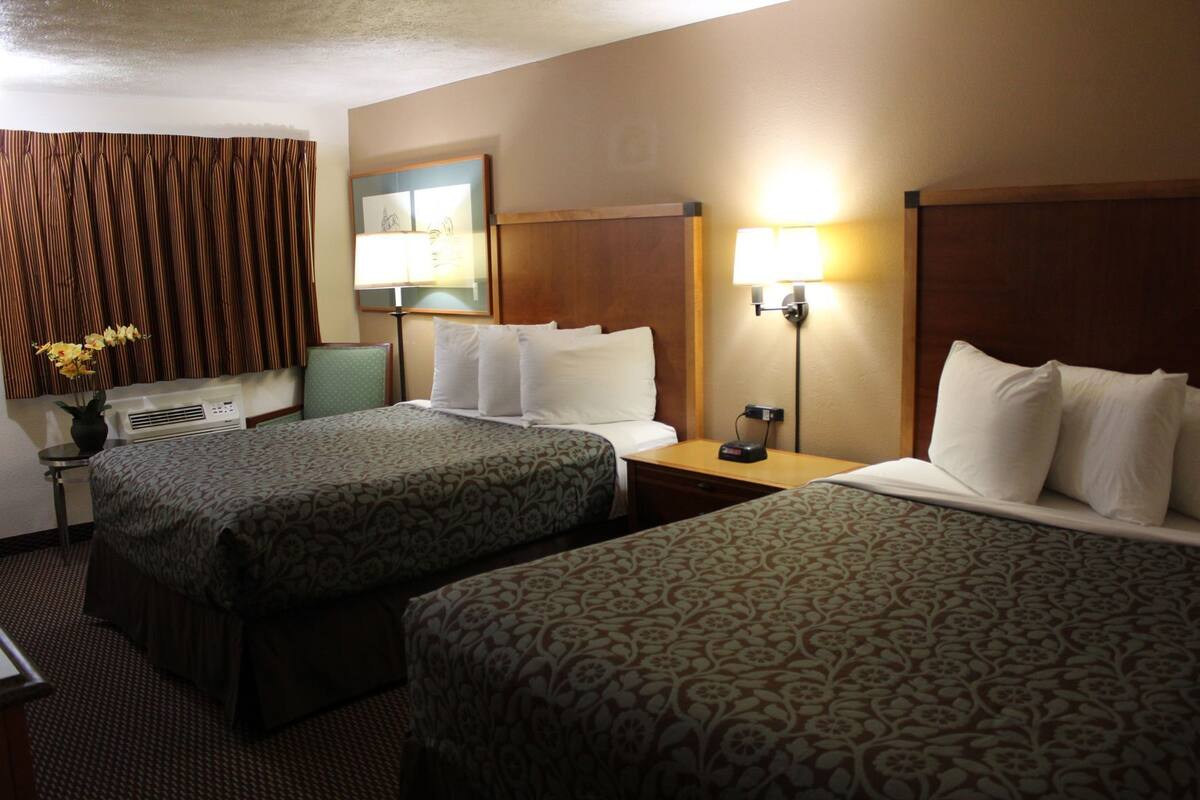 A hotel room with two beds, a nightstand, a lamp, a wall-mounted picture, and a small table with a vase of flowers.