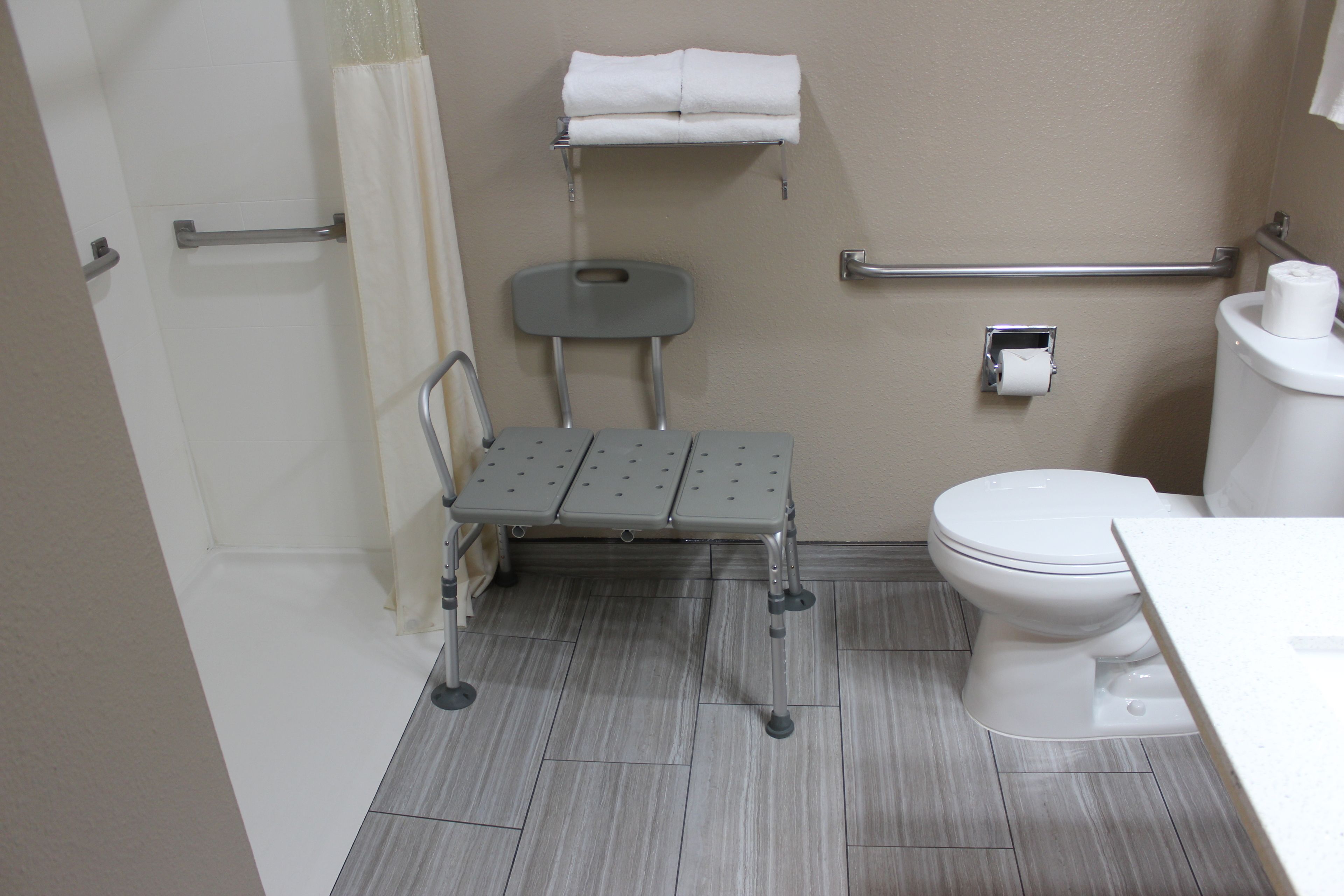 Un baño con inodoro, lavamanos, zona de ducha y barra de apoyo.