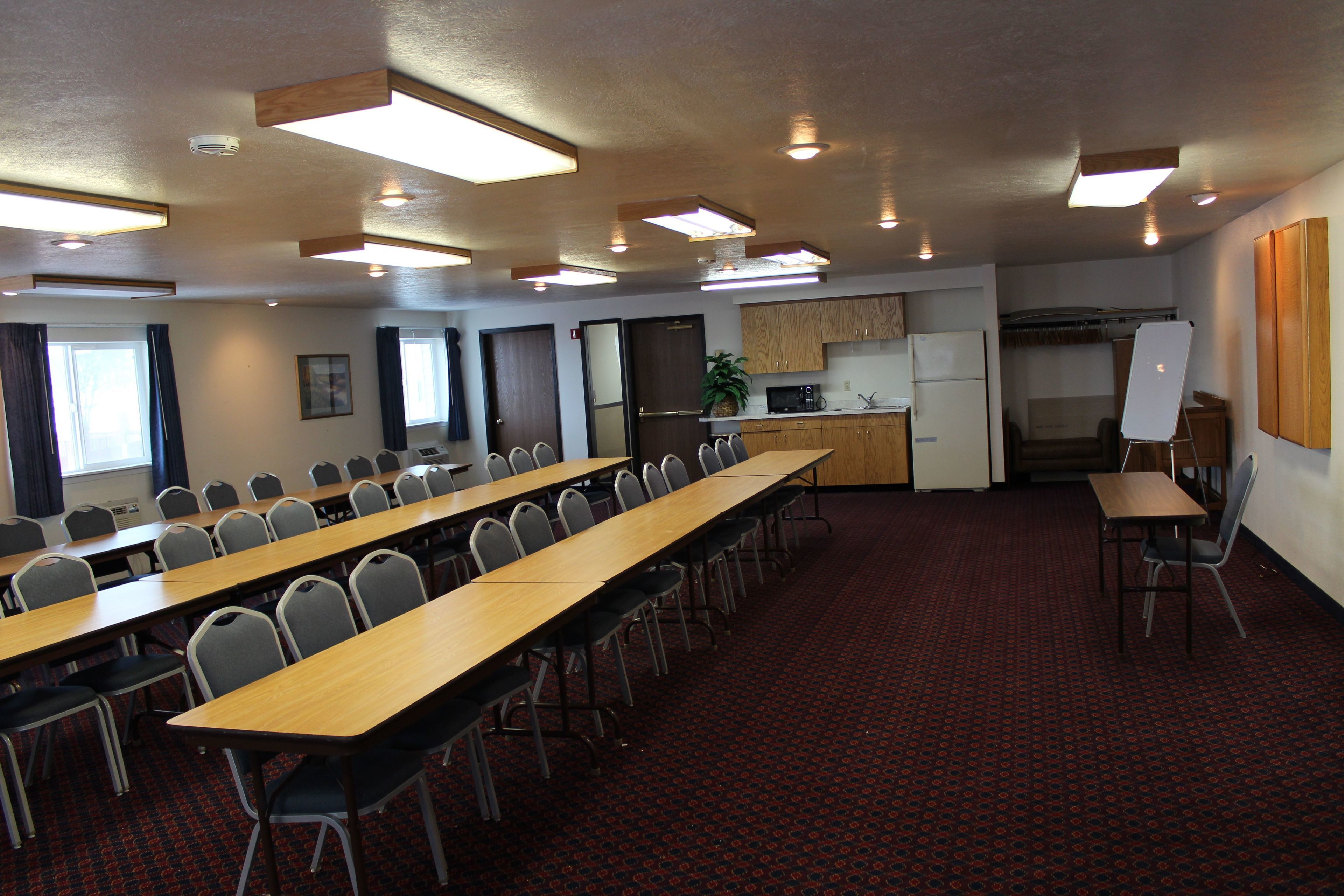 Une salle de conférence équipée d’une longue table, de chaises, d’un coin cuisine et d’un tableau blanc.