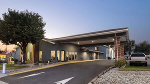 A modern building with a covered entrance, a tree in front, and a paved driveway with directional arrows.