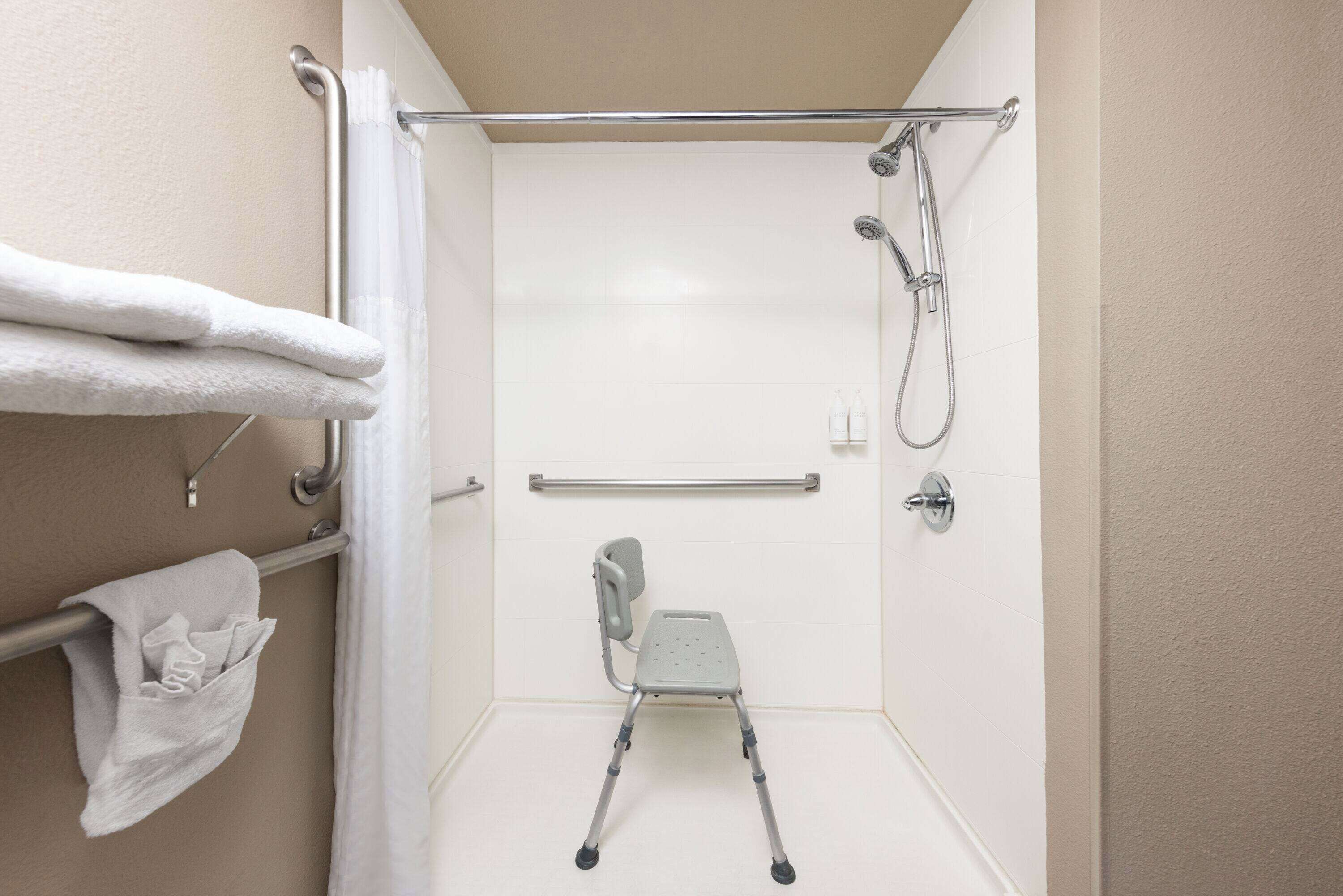 Un espace douche équipé d’une barre d’appui, d’un siège de douche et d’un porte-serviettes avec des serviettes.