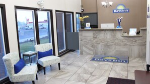 A Days Inn reception area with a marble reception desk, two patterned armchairs, a large window offering a view of a parking lot, and a chandelier.