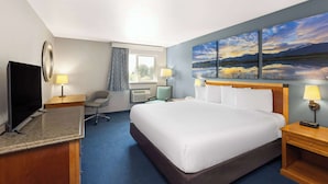 A hotel room with a large bed, a desk with a computer, a chair, a TV, and a painting of a landscape on the wall.