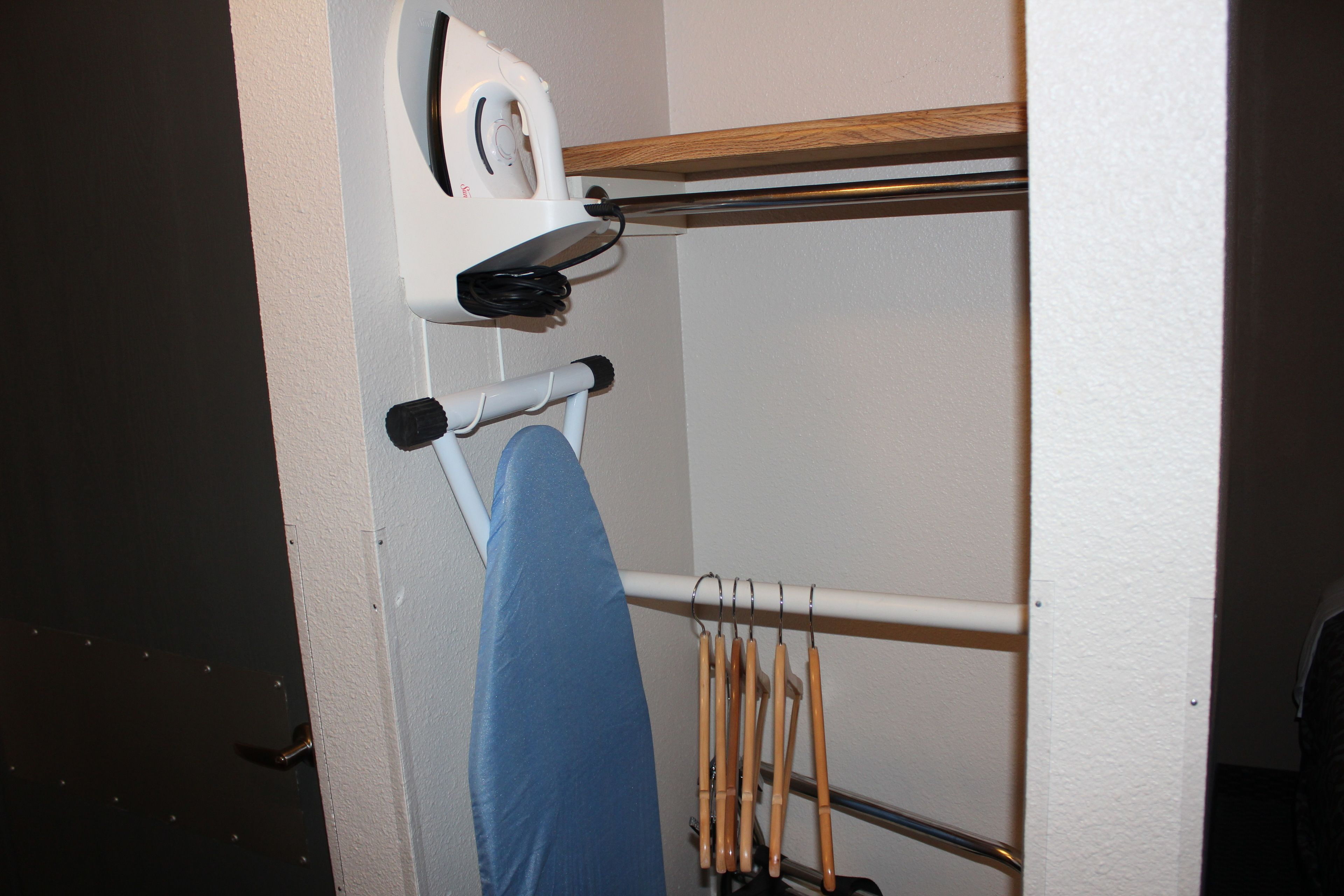 A corner of a room with a white wall, a wooden shelf, and a hanging rack with wooden handles.