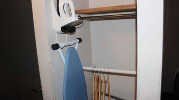A corner of a room with a white wall, a wooden shelf, and a hanging rack with wooden handles.