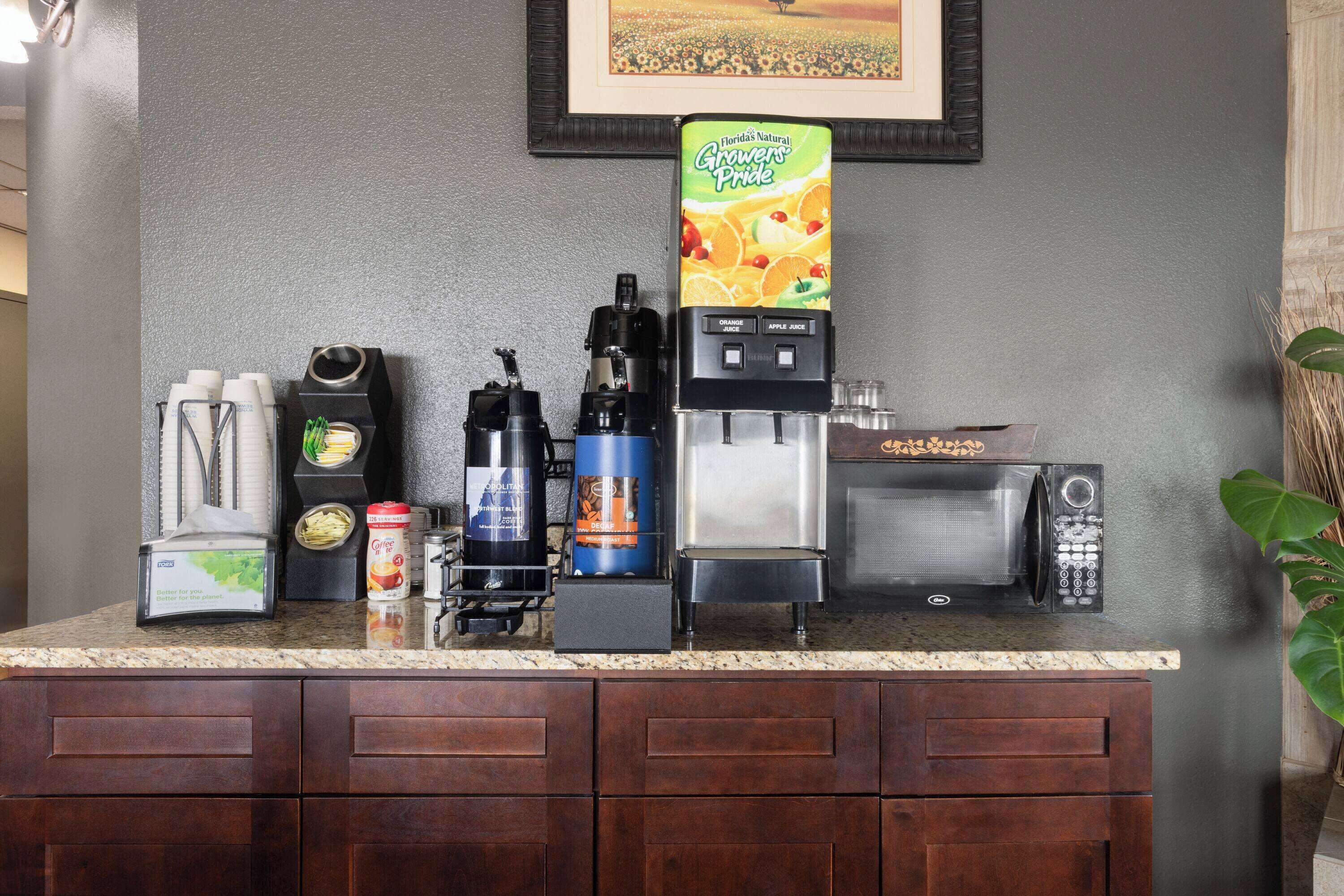 Una encimera de cocina con varios electrodomésticos, como una cafetera, un microondas y un dispensador de zumo.