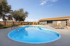 A swimming pool with a wooden deck, lounge chairs, and a covered area.