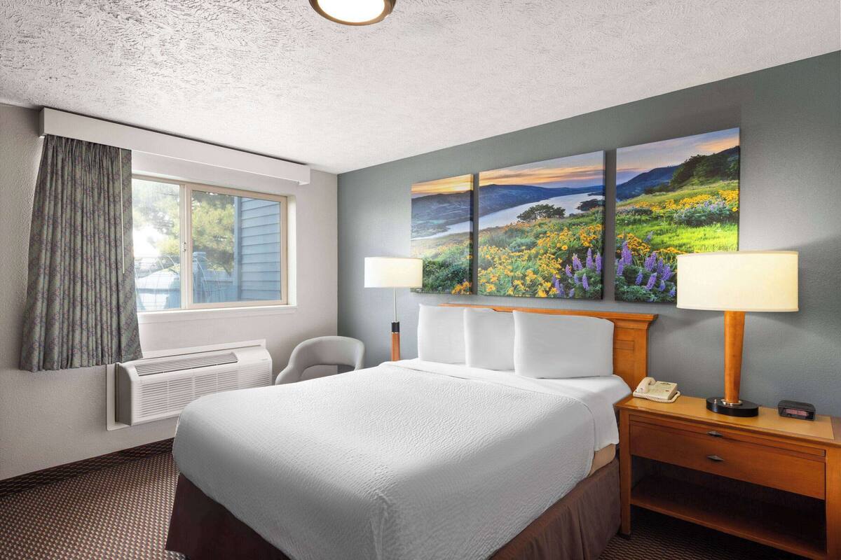 A hotel room with a large bed, two bedside lamps, a desk with a telephone, and a window with curtains.