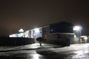 A two-story motel with a covered parking area and a small tree in front.