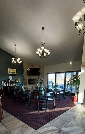 A spacious dining area with multiple tables and chairs, a chandelier, and a large window offering a view of the outdoors.