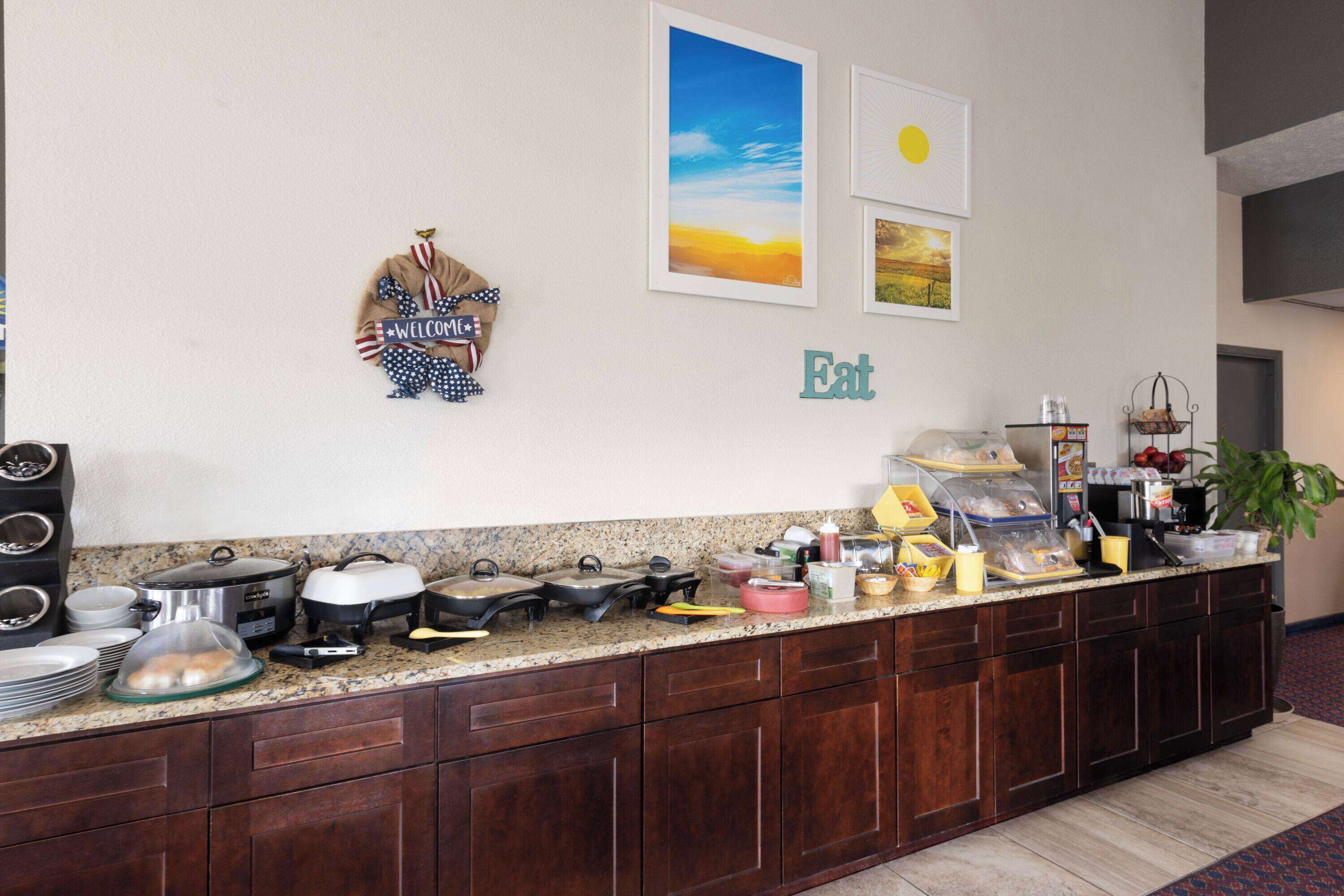 Un comptoir de cuisine avec divers appareils et aliments, une pancarte « Bienvenue » et une autre pancarte « À table » accrochée au mur.