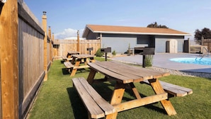A backyard with picnic tables, a swimming pool, and a house with a tiled roof.