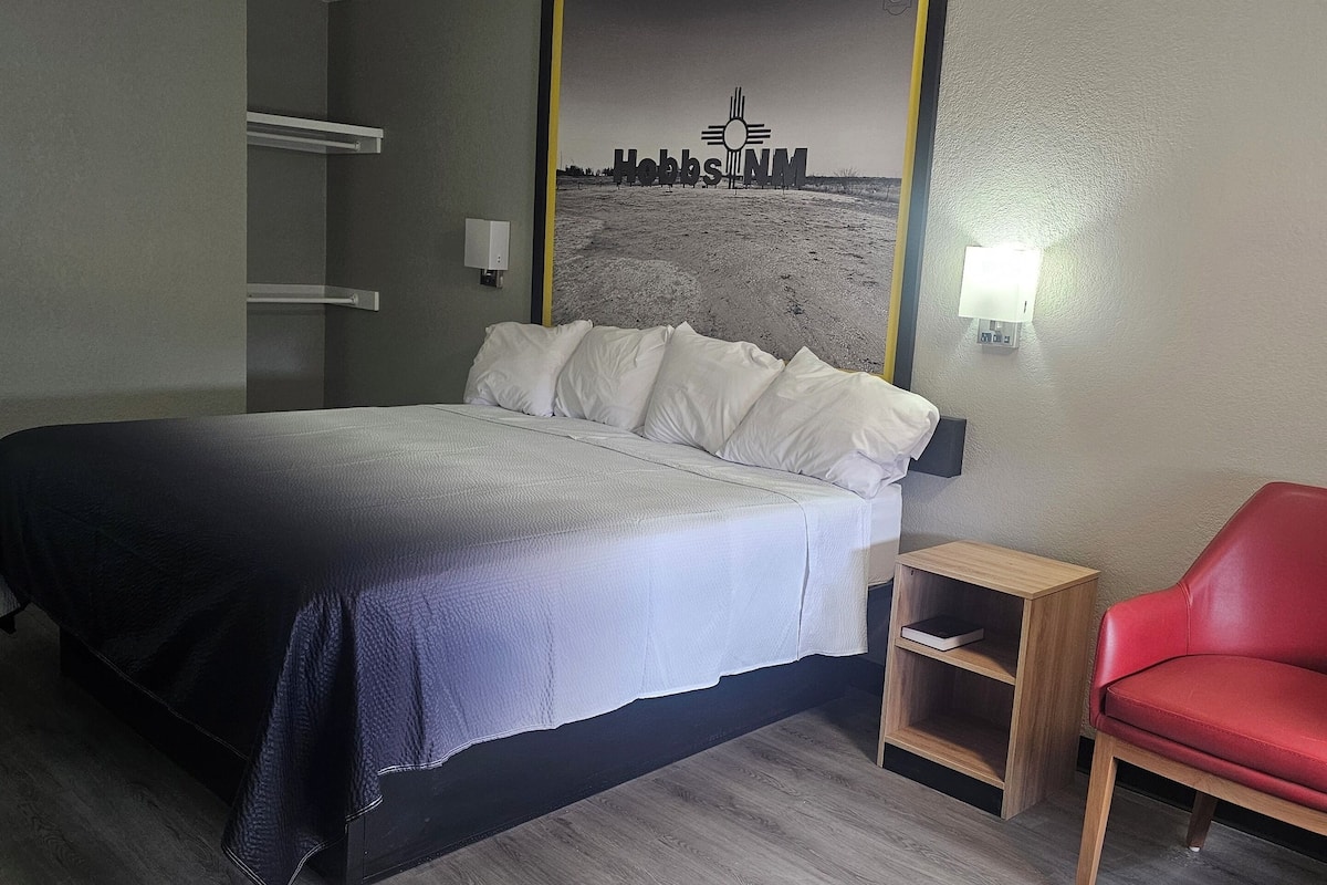 Een hotelkamer met een bed, een rode stoel, een nachtkastje en een lamp aan de muur.
