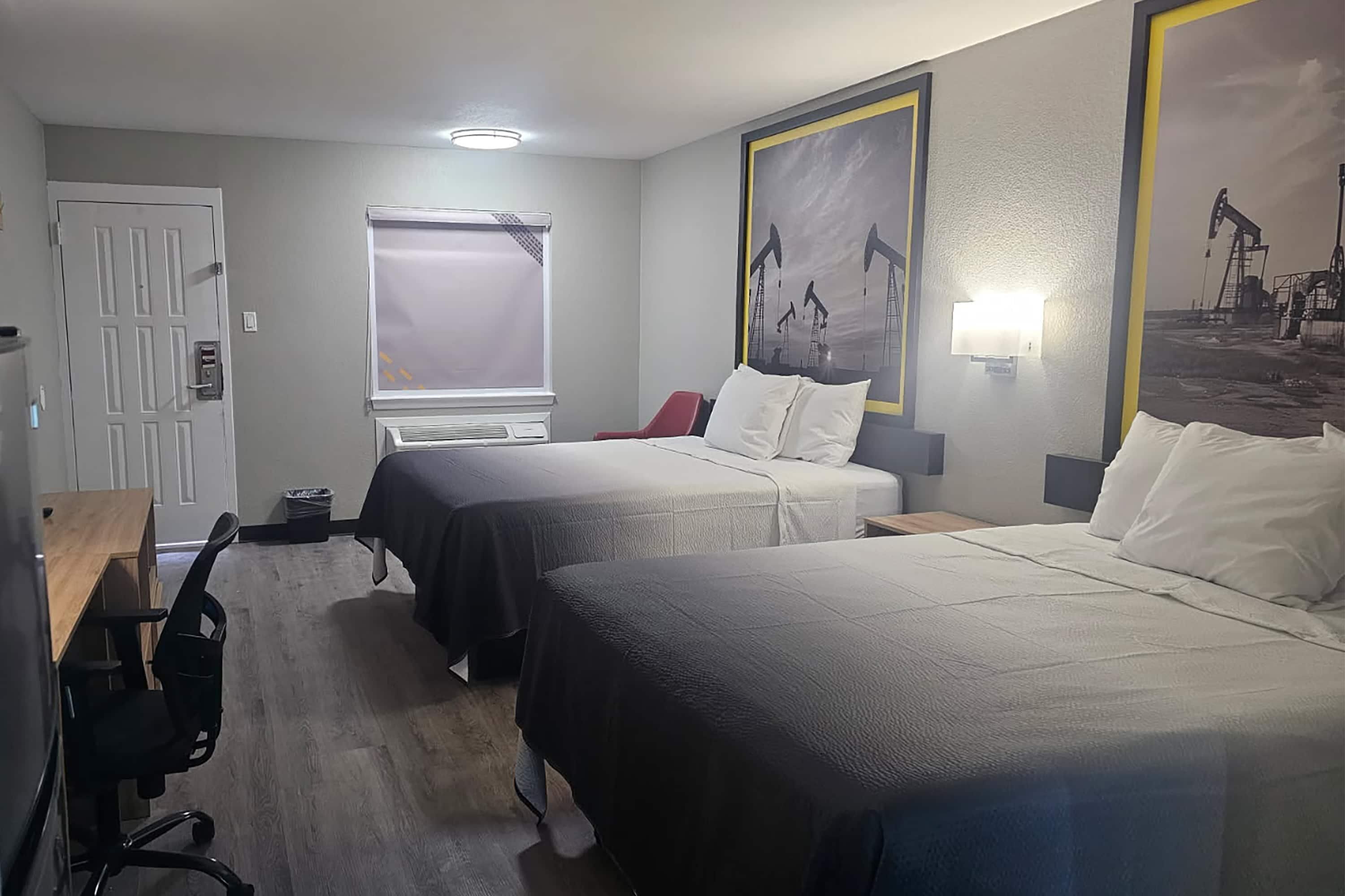 Une chambre d’hôtel avec deux lits, un bureau, une chaise, une fenêtre avec des stores et des œuvres d’art accrochées aux murs.