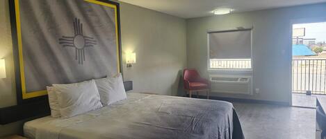 A hotel room with a bed, a red chair, a window with blinds, and a wall-mounted air conditioning unit.
