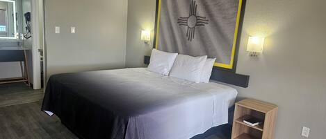 A hotel room with a bed, bedside tables, a wall-mounted artwork, and a bathroom visible through an open door.