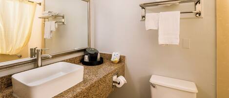 A bathroom with a granite countertop, a white sink, a toilet, a towel rack, and a mirror.