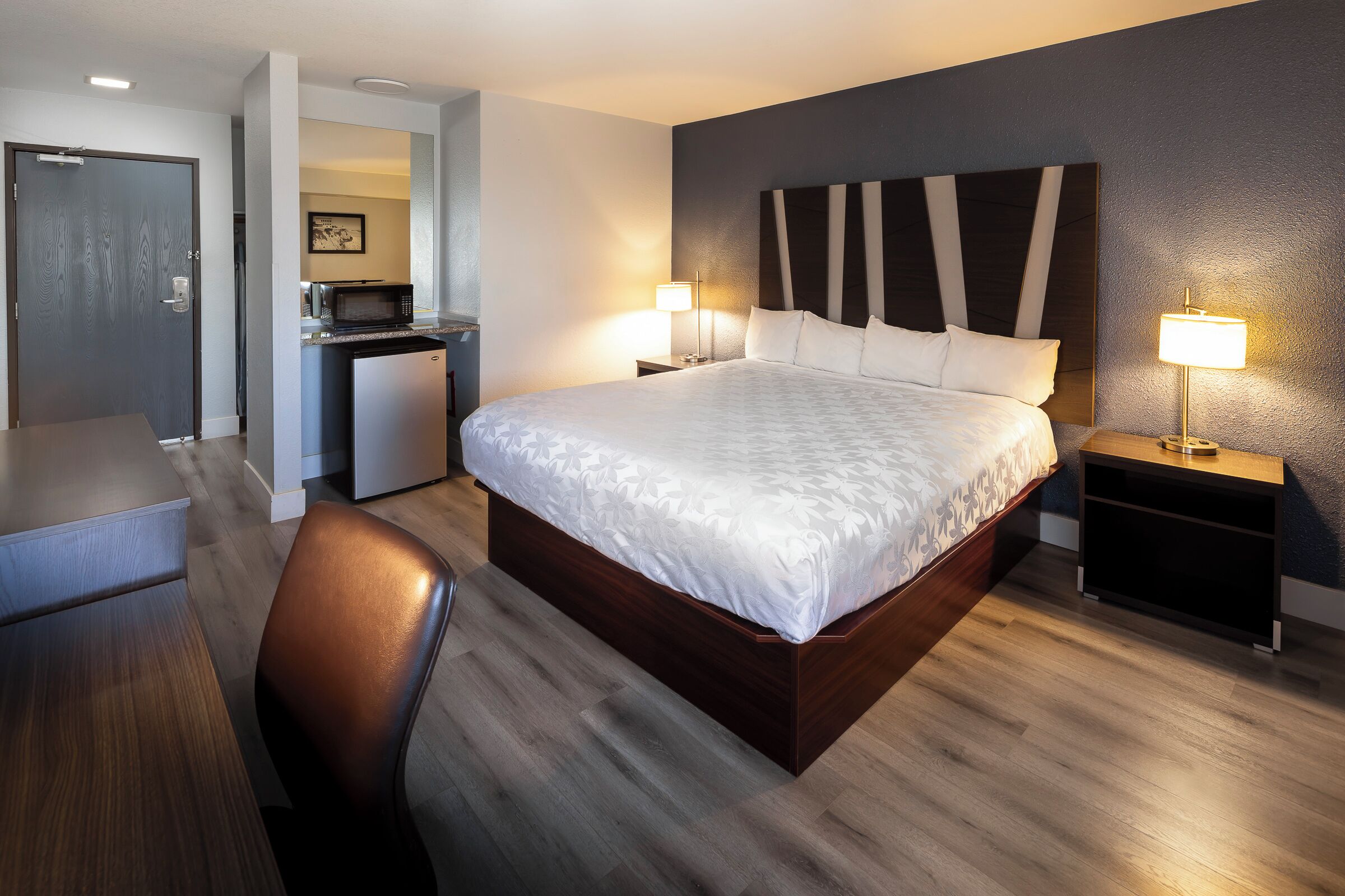 Moderni hotellihuone, jossa on suuri sänky, työpöytä ja mikroaaltouuni nurkassa.