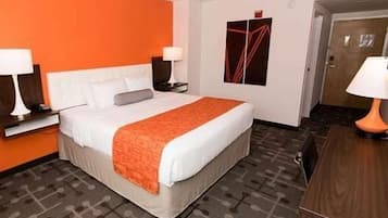 A hotel room with a bed, two bedside tables with lamps, a wooden desk, and a patterned carpet.