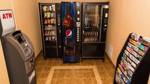 Zona de venta con Pepsi, Coca-Cola y otras bebidas, un cajero automático y una estantería con revistas.