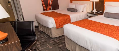 A hotel room with two beds, a desk, a chair, a lamp, and a wall with geometric artwork.