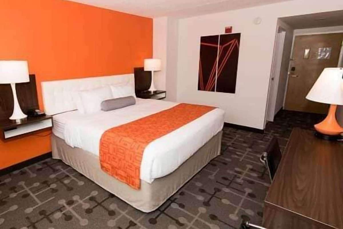 Una habitación de hotel con una cama, dos mesitas de noche con lámparas, una mesita auxiliar, un aparador y una puerta.