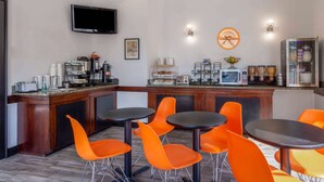 Un área de cocina moderna con barra, sillas color naranja, televisor y diversos electrodomésticos.