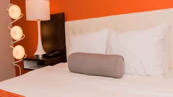 Et hotelværelse med en hvid seng, en grå pude, en hvid lampe og et natbord med en telefon.