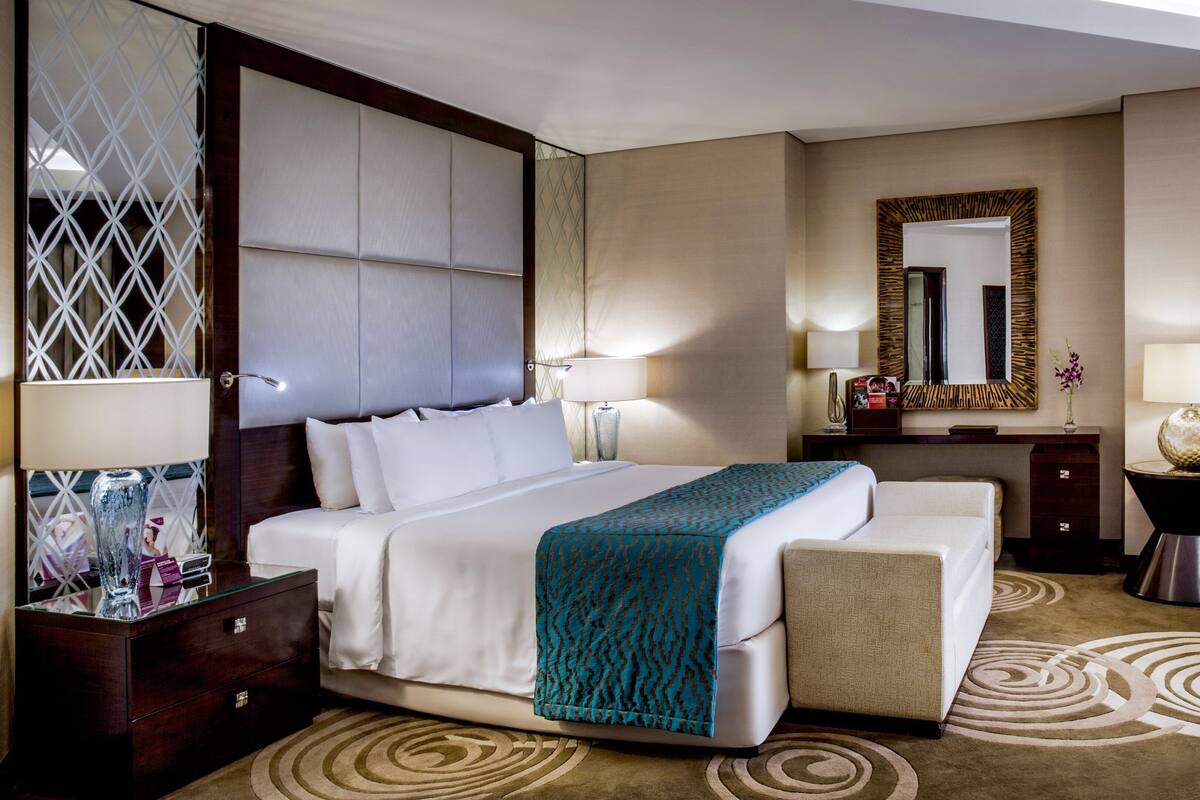 Une chambre d’hôtel avec un grand lit, deux tables de chevet, un canapé, un miroir et un panneau décoratif mural.