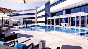A pool area with lounge chairs and umbrellas, a lifebuoy, and a building with 'CROWNE PLAZA' signage. - Crowne Plaza Dubai Deira by IHG (Dubai)