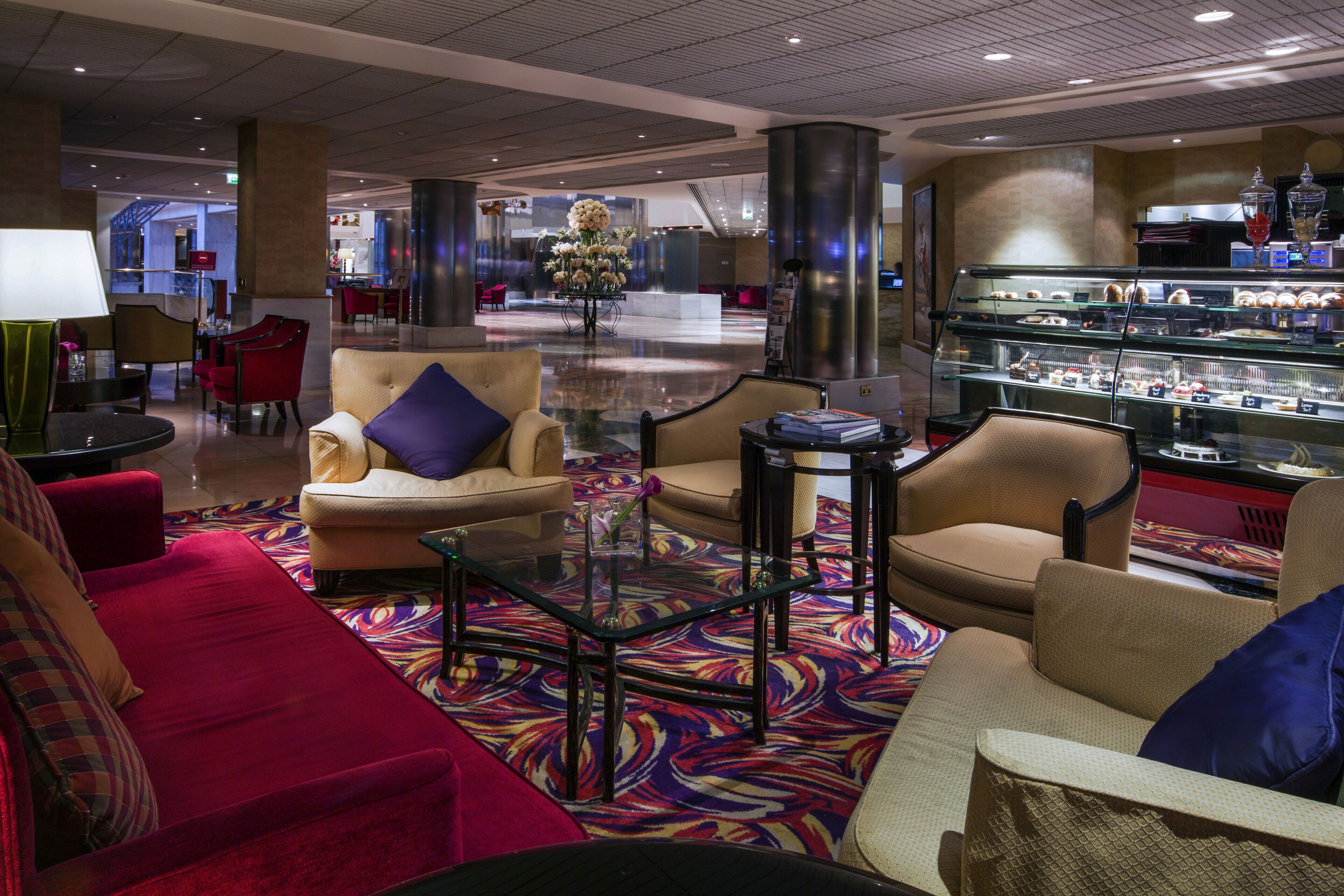 Un hall de hotel con zonas de estar, un mostrador de recepción y una vitrina con pasteles.