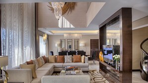 A spacious living room with a large sofa, a coffee table, and a television. There is a chandelier, a mirror, and a decorative wall panel. - Crowne Plaza Dubai Deira by IHG (Dubai)