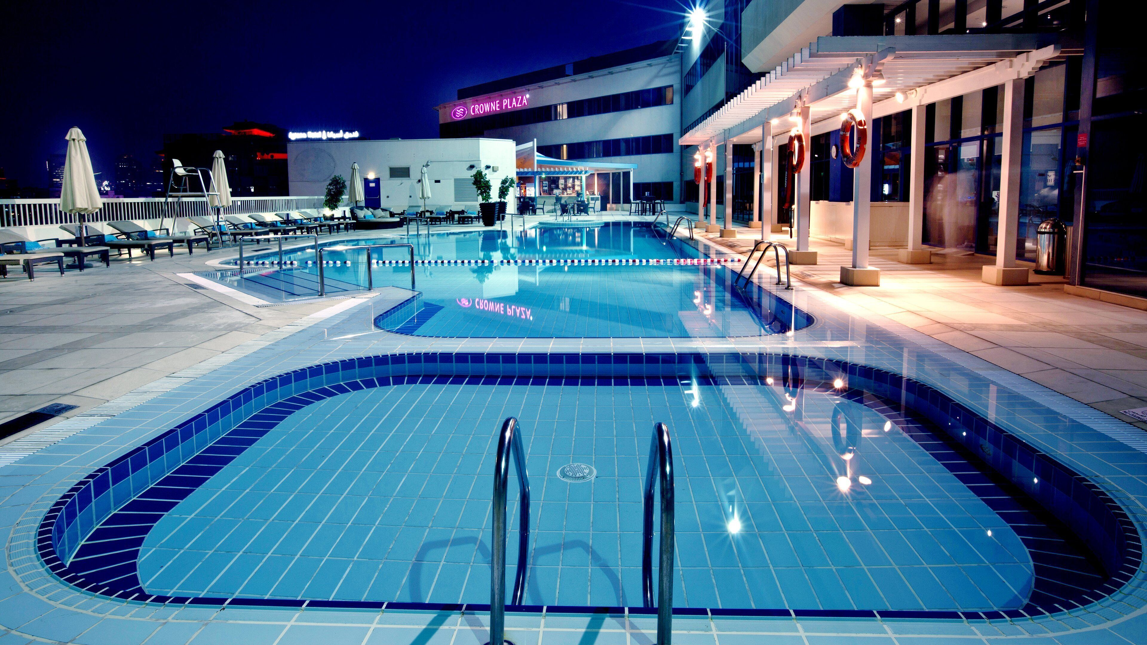 A swimming pool area with lounge chairs and umbrellas, a covered seating area, and a building with signage.