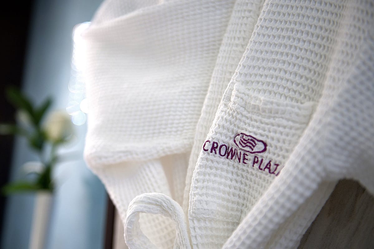 Une serviette blanche avec le texte « CROWNE PLAZ » et un logo, suspendue à un porte-serviettes.